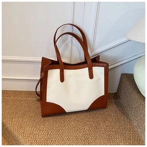 Détail du sac cabas contrasté avec corps en toile et garnitures en cuir marron