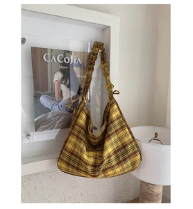 Detail of yellow plaid tote bag featuring pleated shoulder strap and side ribbon bow