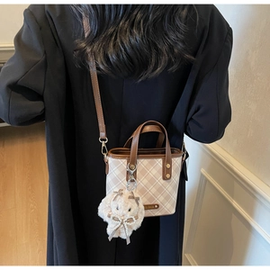 Detail of checkered bucket bag featuring brown leather trim and cute rabbit plush charm