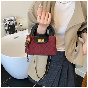 Close-up of wine red quilted fabric bag with black leather handle and golden twist lock