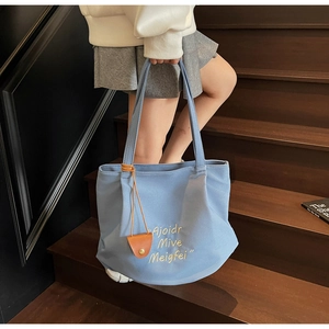 Close-up of blue canvas tote bag featuring white embroidery and brown leather pendant charm