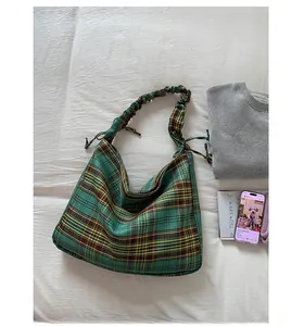 Detail of green plaid tote bag with pleated handle on a white textured background