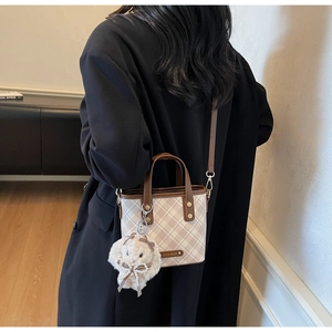 Detail of a plaid bucket bag with a plush bunny charm on a black coat outfit