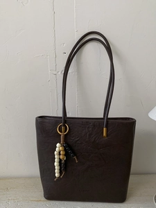 Dark brown pleated leather tote bag with elegant beaded charm on a stone surface