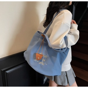 Detail of blue canvas tote bag with yellow letter embroidery and brown leather trim