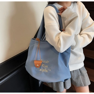 Detail of blue canvas tote bag featuring embroidered lettering and brown leather charm