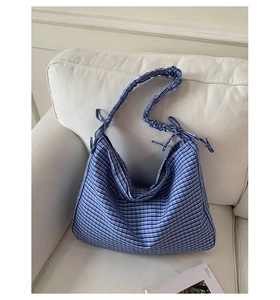 Detail of blue plaid tote bag with ruffled strap and side bow knots on a white sofa