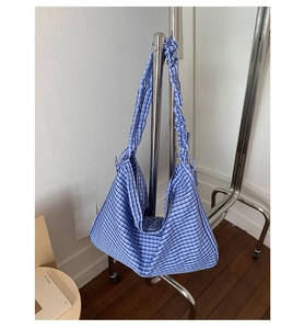 Detail of blue plaid tote bag featuring ruffled shoulder strap and soft fabric texture