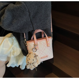 Detail of pink plaid crossbody bag with plush charm shown on a model against wood steps