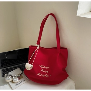 Detail of red canvas tote bag with white embroidery and small wallet charm on shoulder strap