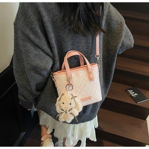 Detail of a pink and white checkered bucket bag with a plush bunny charm and pearl bow