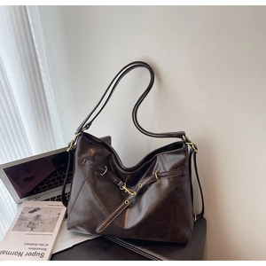 Close-up of vintage dark brown hobo bag with gold buckle next to a laptop