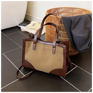 Vue détaillée du sac cabas en toile bicolore avec anses en cuir marron sur sol sombre