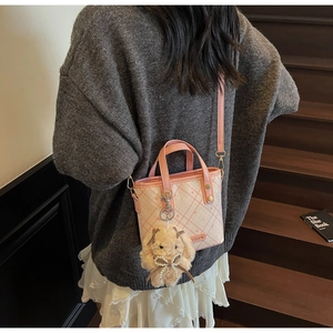 Detail of pink plaid PU leather tote bag with plush bunny charm on a model