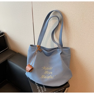 Detail of blue canvas tote bag featuring yellow cursive embroidery and brown leather charm