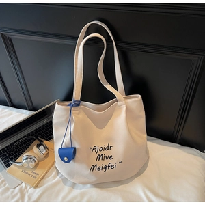 Detail of a large cream canvas tote bag with black lettering and a blue charm pendant