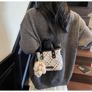 Detail of checkered tote bag with plush bunny charm worn by model in casual setting