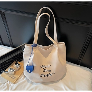 Detail of a beige canvas tote bag with black lettering and a blue pendant accessory