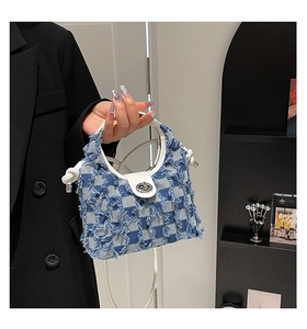 Detail of blue plaid denim bucket bag with frayed edges and white leather handles