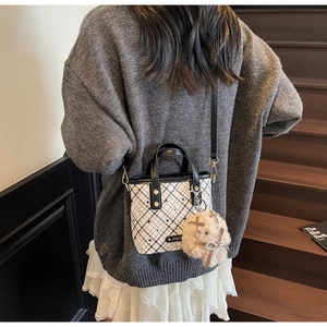 Detail of crossbody bucket bag featuring black and white patterns and plush charm on stairs