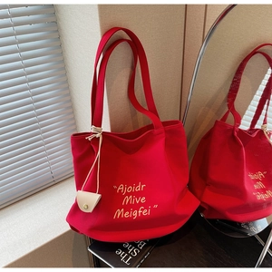 Macro detail of red canvas tote bag with yellow lettering and a small white pouch charm
