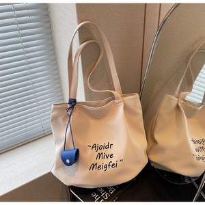 Detail of beige canvas tote bag featuring black lettering and a blue mini pouch charm