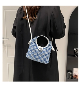 Detail view of plaid denim bucket bag with frayed edges and white leather strap