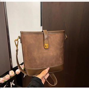 Detail of dark brown suede bucket bag with gold metal buckle and leather shoulder strap