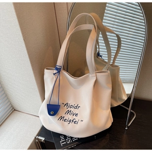 Detail of cream tote bag with blue charm and artistic lettering on a textured surface