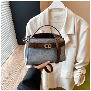 Detail of blue denim crossbody bag with brown leather trim and metal double buckles