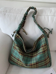 Vintage green plaid tote bag with pleated straps and bow detail on a white sofa