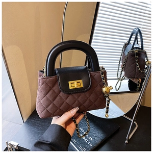 Detailed close-up of quilted coffee brown bag with gold ball charm and chain strap