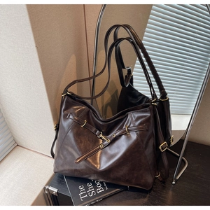Detail of dark brown leather tote bag showing glossy texture and vintage gold buckle