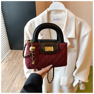 Detailed close-up of quilted burgundy suede bag with gold ball chain and turn-lock