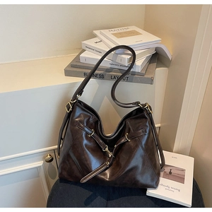 Detail of dark brown leather tote bag with gold ring buckle on velvet seat with books