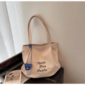 Close-up of beige tote bag featuring black artistic lettering and a blue mini card holder charm