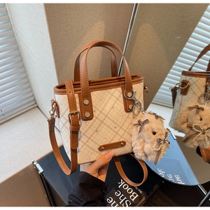 Detail showing the brown plaid pattern and plush rabbit charm on a cream bucket bag