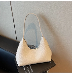 Close-up of a cream pebble leather hobo shoulder bag placed on a black design book