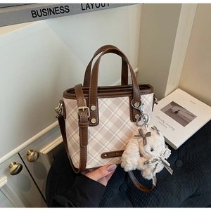 Detail of beige plaid bucket bag with brown leather trim and cute rabbit pendant