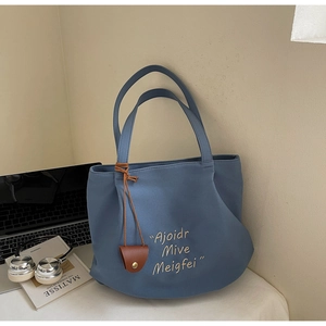 Detail of blue canvas tote bag with embroidery and brown leather charm in office setting