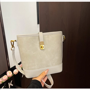 Detail of grey bucket bag showing golden metal lock and textured matte finish leather