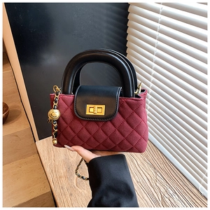 Detail of burgundy quilted bag with black leather handle and golden chain ball ornament