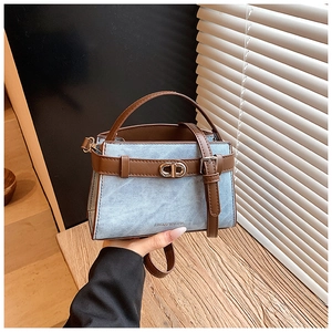 Macro detail of blue denim handbag with brown leather stitching and metallic buckle