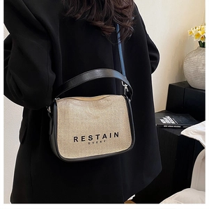 Chic beige canvas and black leather crossbody bag styled on a person in a modern interior