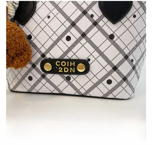 Close-up of white plaid bucket bag with gold rivets and brown faux fur charm