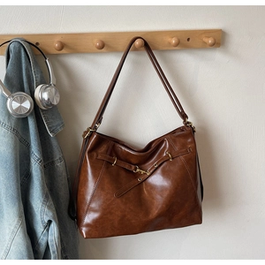 Close-up of vintage brown leather tote bag showing crossbody strap and metal buckle detail