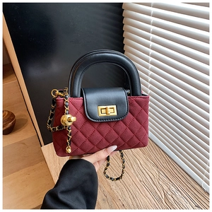 Detail of burgundy suede quilted handbag with black leather handle and gold twist lock