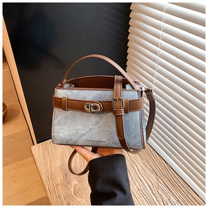 Detailed view of blue denim and brown leather bucket bag with metallic buckle