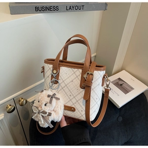 Detail of grid patterned crossbody bag with a plush bunny charm and brown leather trim