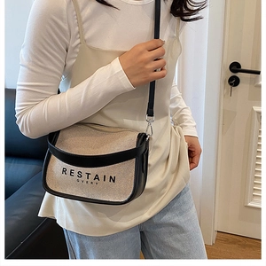 Detailed side view of a beige canvas crossbody bag with black leather trim on model